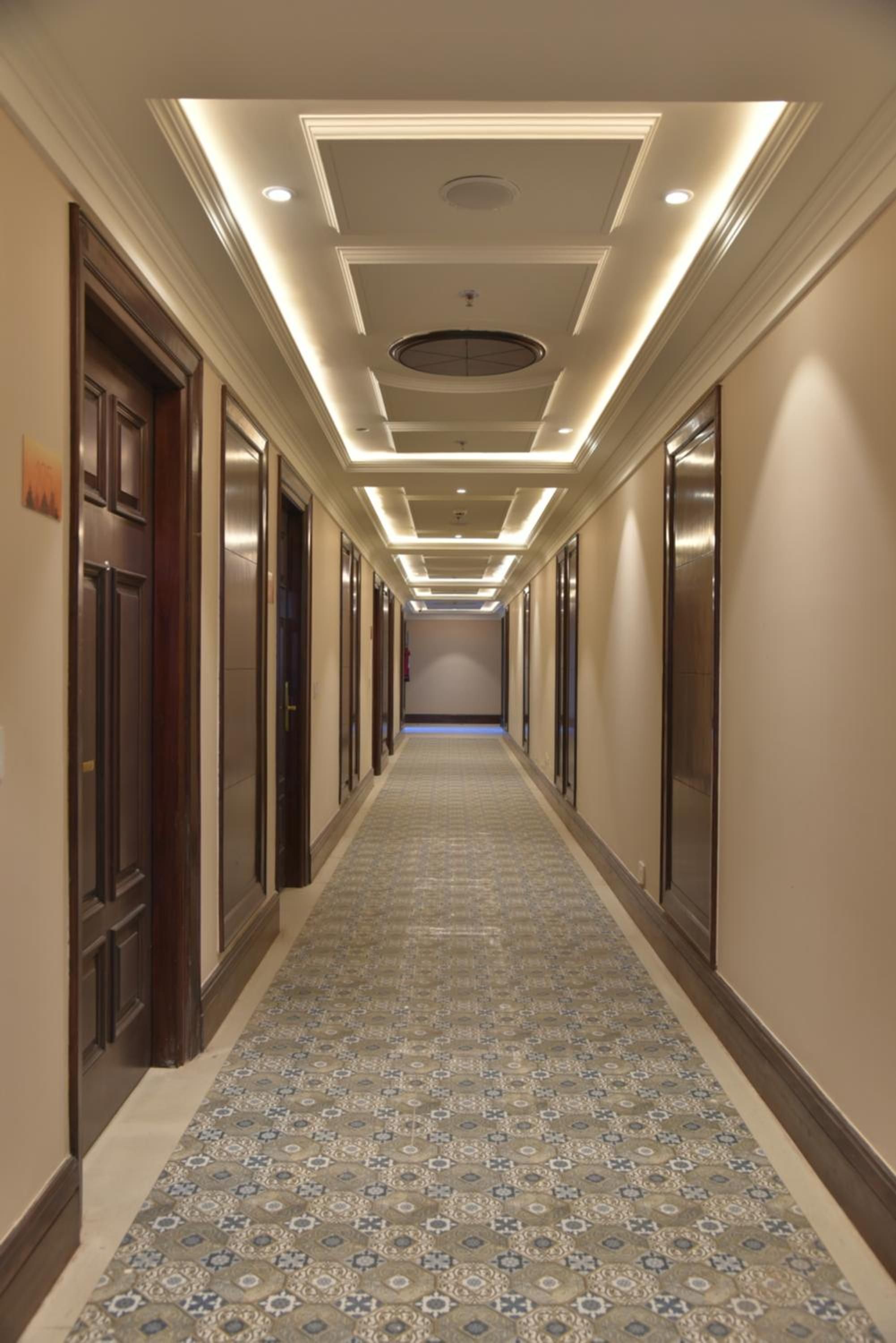 A hotel corridor with a patterned carpet, recessed lighting, and doors on both sides.