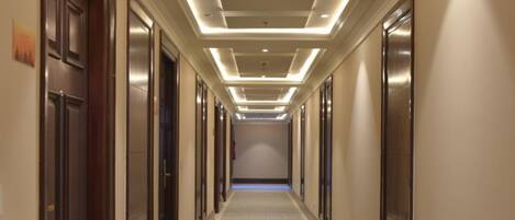 A hotel corridor with a patterned carpet, recessed lighting, and doors on both sides.