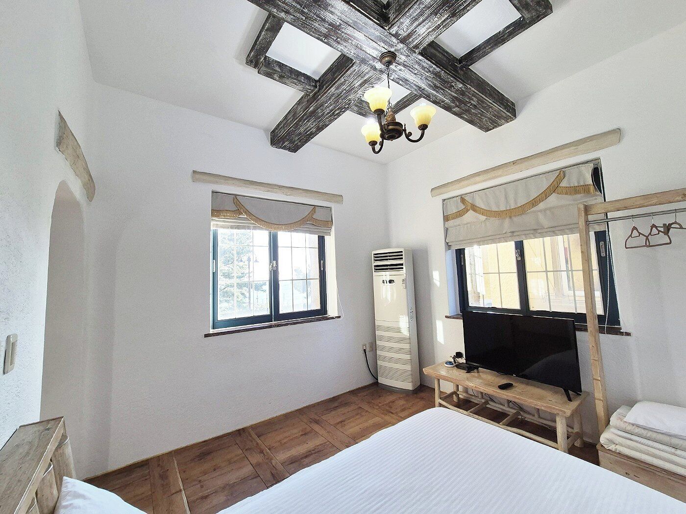 Un dormitorio con una cama grande, techo de madera, una ventana, aire acondicionado y una televisión sobre un mueble de madera.