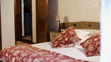Ein Schlafzimmer mit Holz-Kopfteil, einem Bett mit roten Blumenmotiven, einem Nachttisch mit Lampe und einer teilweise geöffneten Tür zu einem anderen Raum.