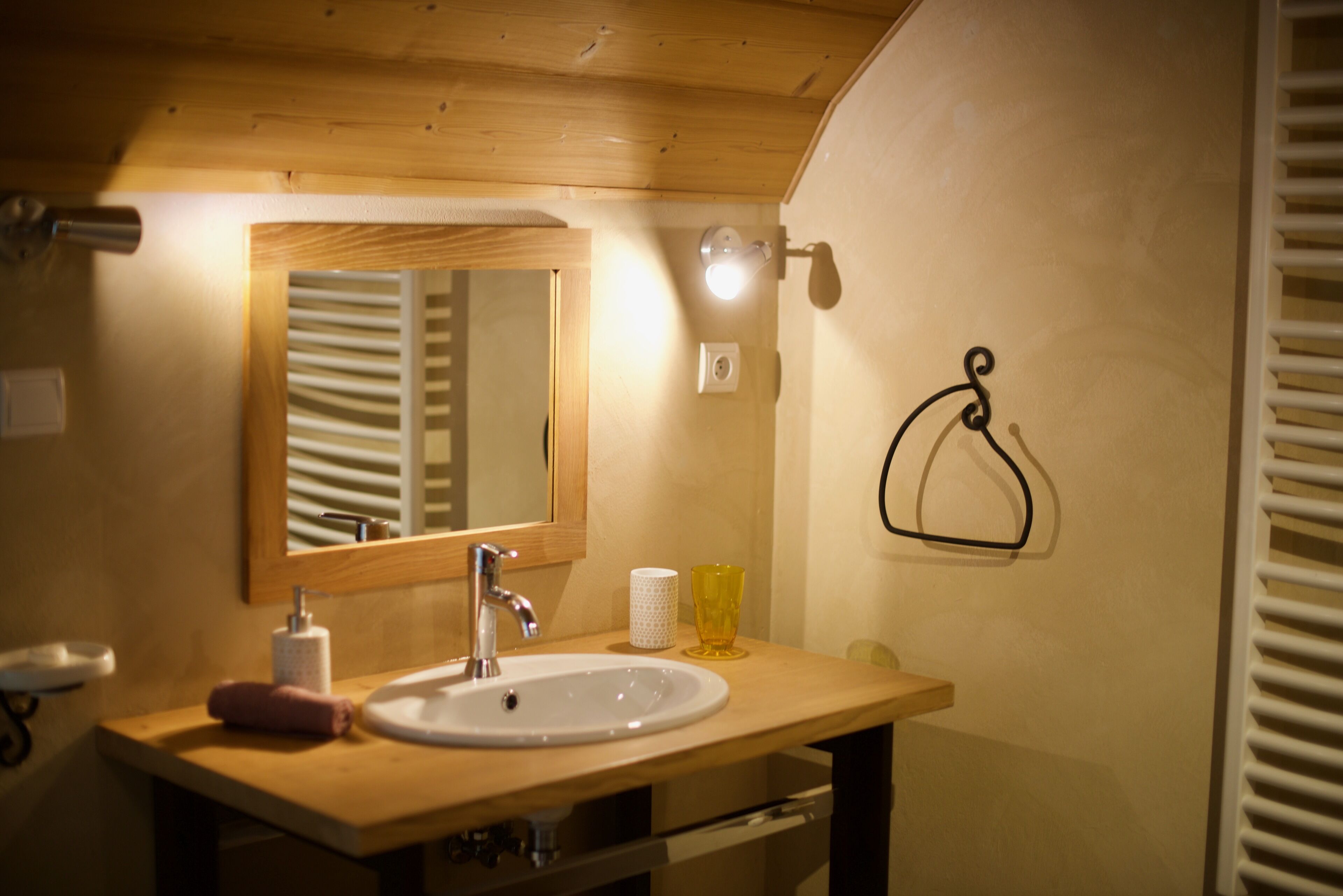 Un bagno con un mobile bagno in legno, un lavandino bianco, uno specchio, un asciugamano e un bicchiere.