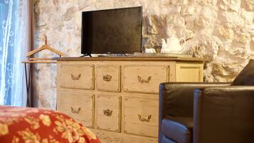 Une pièce avec un téléviseur posé sur une commode en bois, un fauteuil en cuir noir et une couvre-lit à motifs floraux rouges.