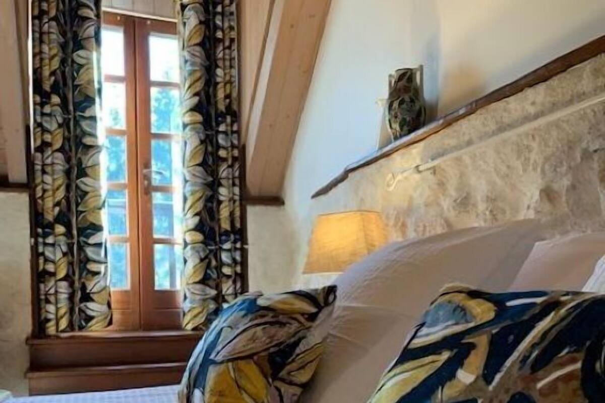 Une chambre à coucher avec un lit, des rideaux à motifs, un plafond en bois et un mur en pierre.