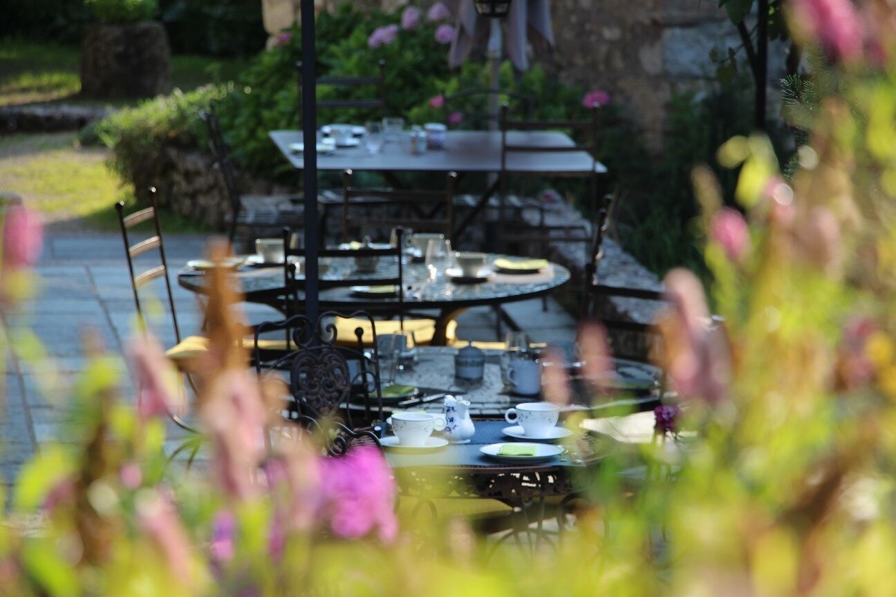An outdoor dining area with round tables and chairs, surrounded by greenery and flowers.