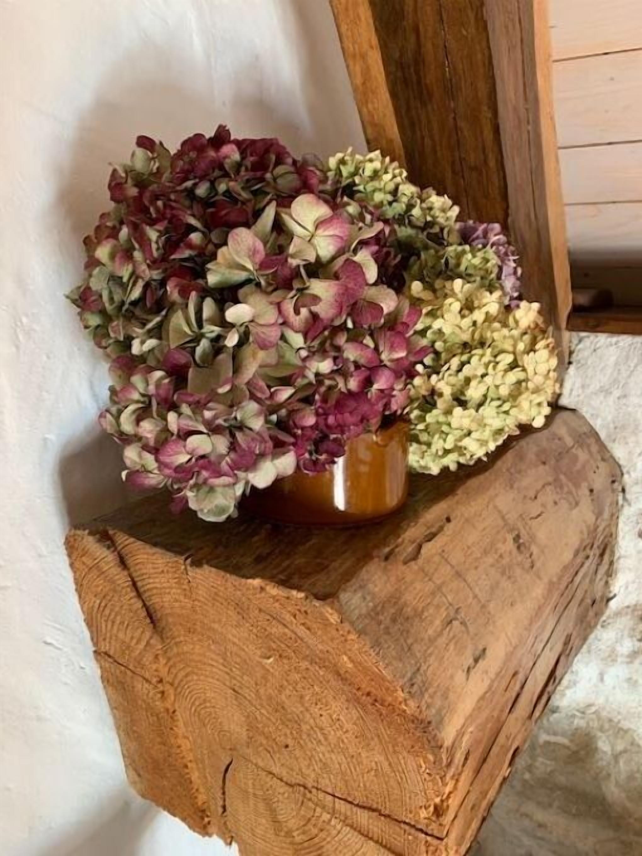 A rustic wooden bench with a vase of hydrangeas.