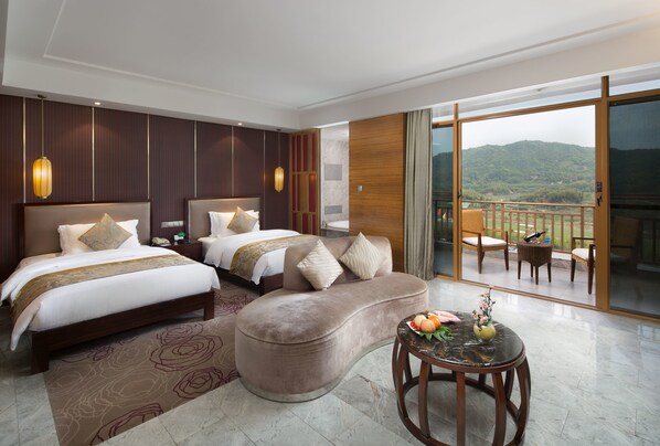 A hotel room with two beds, a sofa, a balcony with outdoor furniture, and a view of the mountains.