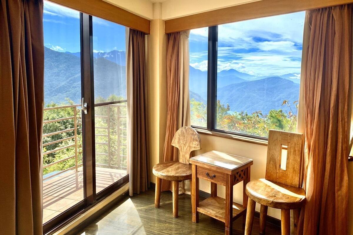 A corner room with large windows, a wooden table, two chairs, and a view of mountains.