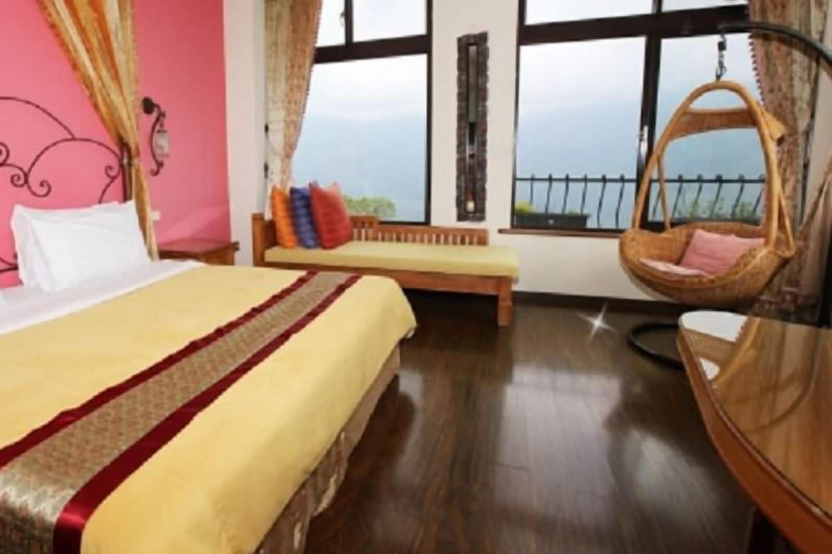 A hotel room with a large bed, a bench, a hanging chair, and a view of the mountains through the window.