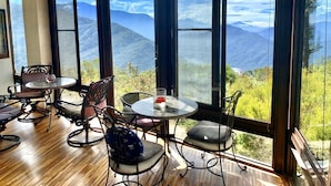 A room with large windows offering a mountain view, wooden flooring, and metal-framed chairs and tables. - Margaret Garden Villa (Ren'ai)