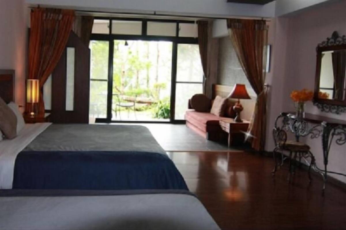 A hotel room with a large bed, a desk with a lamp, a chair, and a view of the outdoors through a glass door.