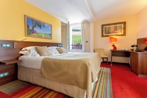 A hotel room with a bed, a desk, a chair, a TV, and a window with a view of a field.