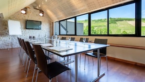 A conference room with a long table, chairs, a whiteboard, and a TV. Large windows offer a view of vineyards. - Hotel Restaurant Famille Bourgeois (Sancerre)