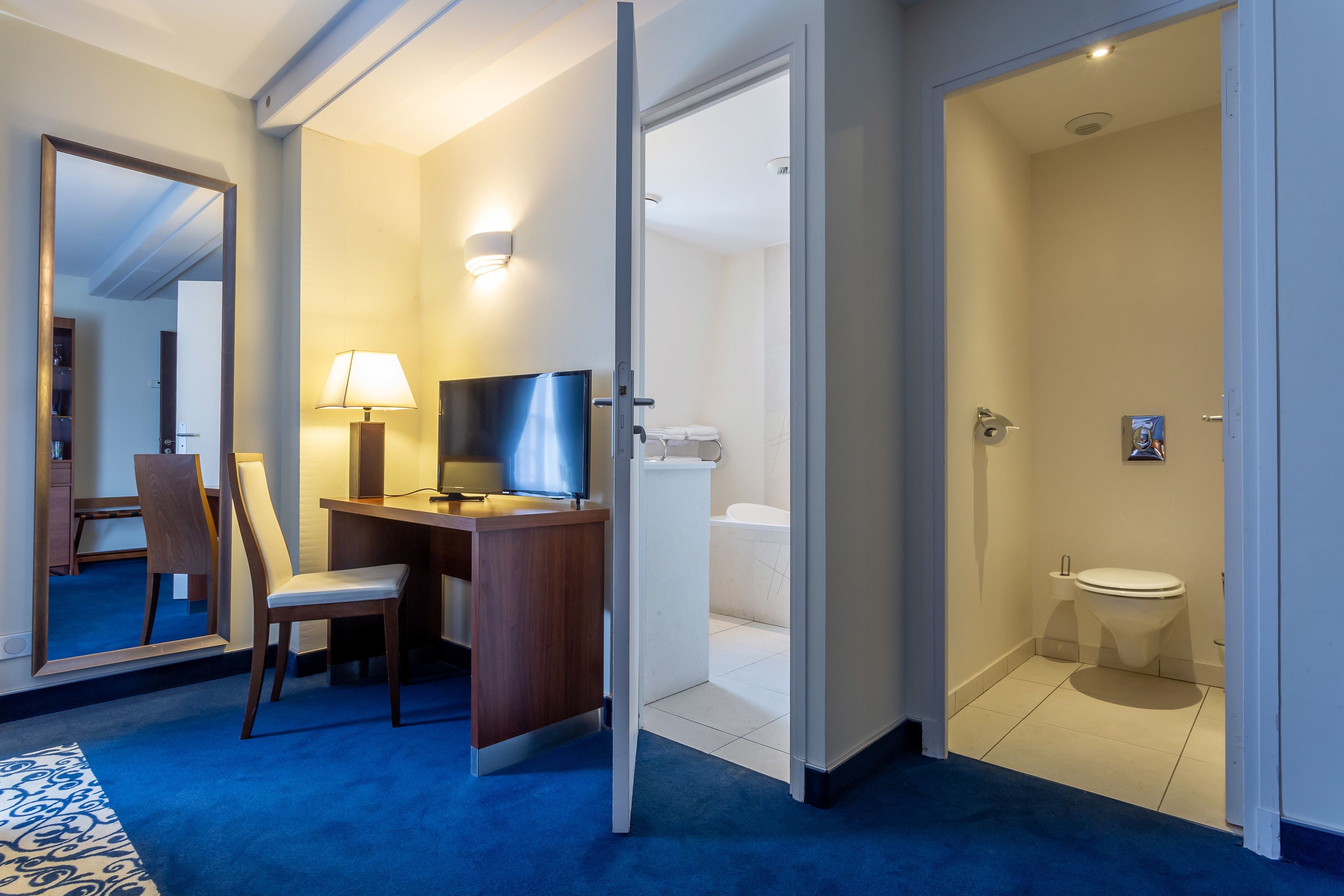 Una habitación de hotel con escritorio, silla, televisor y baño con inodoro y lavamanos.
