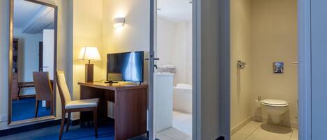 Une chambre d’hôtel équipée d’un bureau, d’une chaise, d’une télévision et d’une salle de bain avec des toilettes et un lavabo.