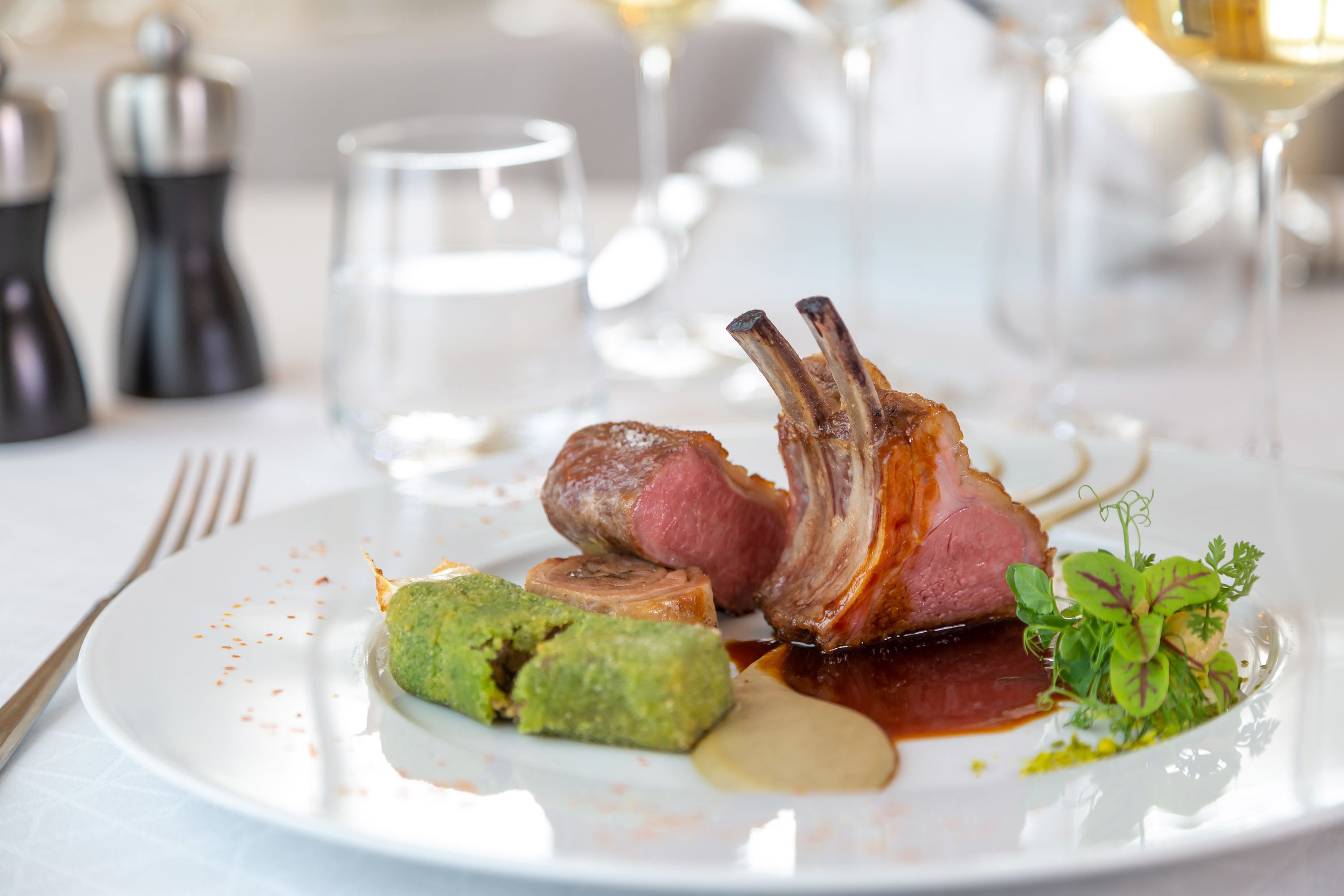 A plate with a lamb chop, a green vegetable, and a sauce.