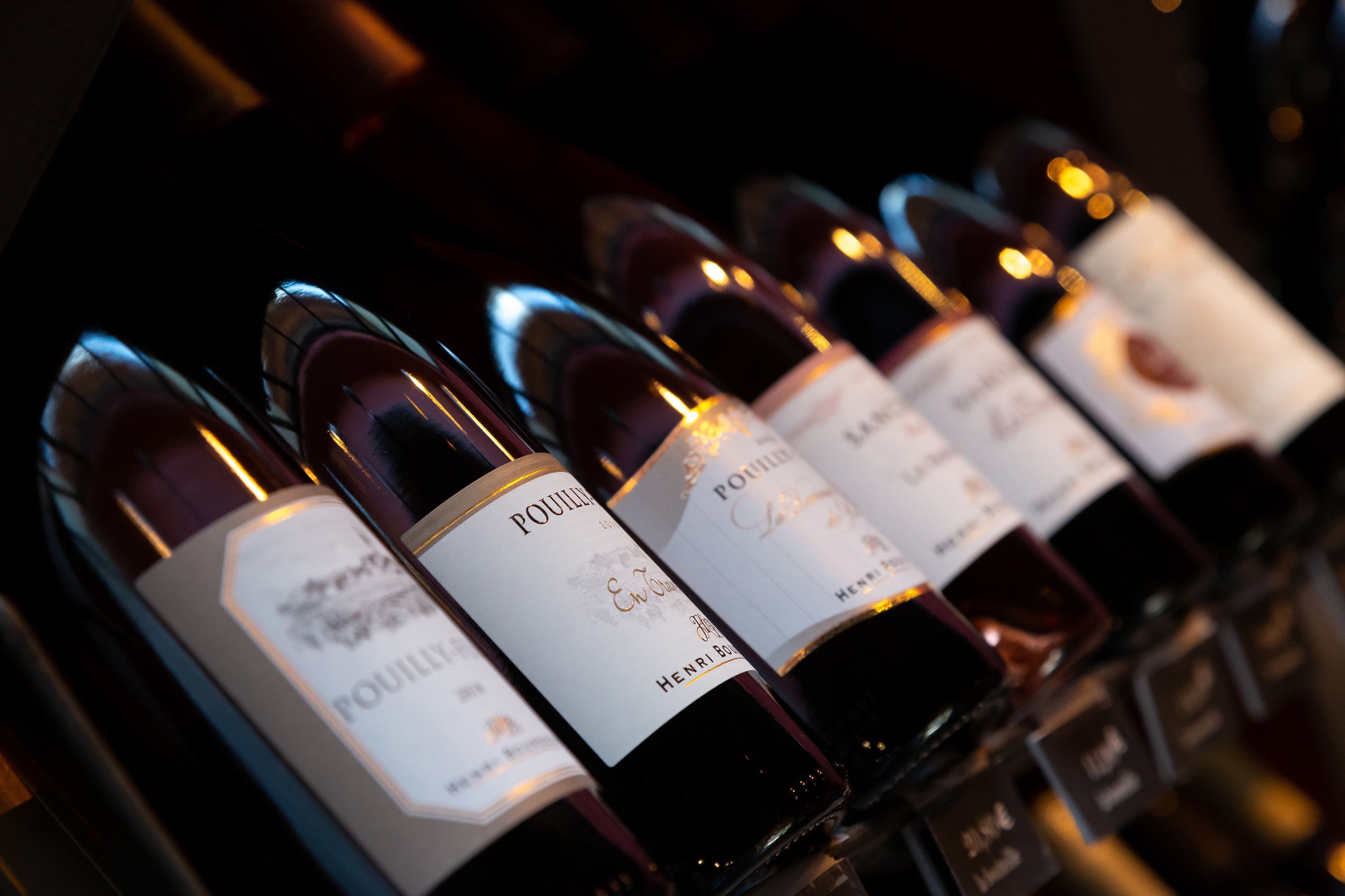 Une rangée de bouteilles de vin, toutes étiquetées, probablement dans une cave à vin ou dans un espace de stockage.