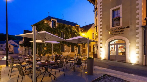 An outdoor café with tables and chairs, a building with a sign reading "Hotel de Charme Restaurant," and a street lamp. - Hotel Restaurant Famille Bourgeois (Sancerre)