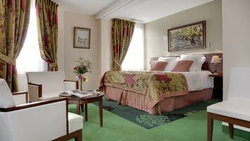 Ein Hotelzimmer mit Bett, zwei Stühlen, einem kleinen Tisch, einer Vase mit Blumen und einem Bild an der Wand.