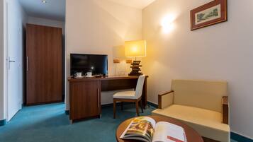 Habitación de hotel con escritorio, silla, sofá, televisión, lámpara y una revista sobre una mesa.