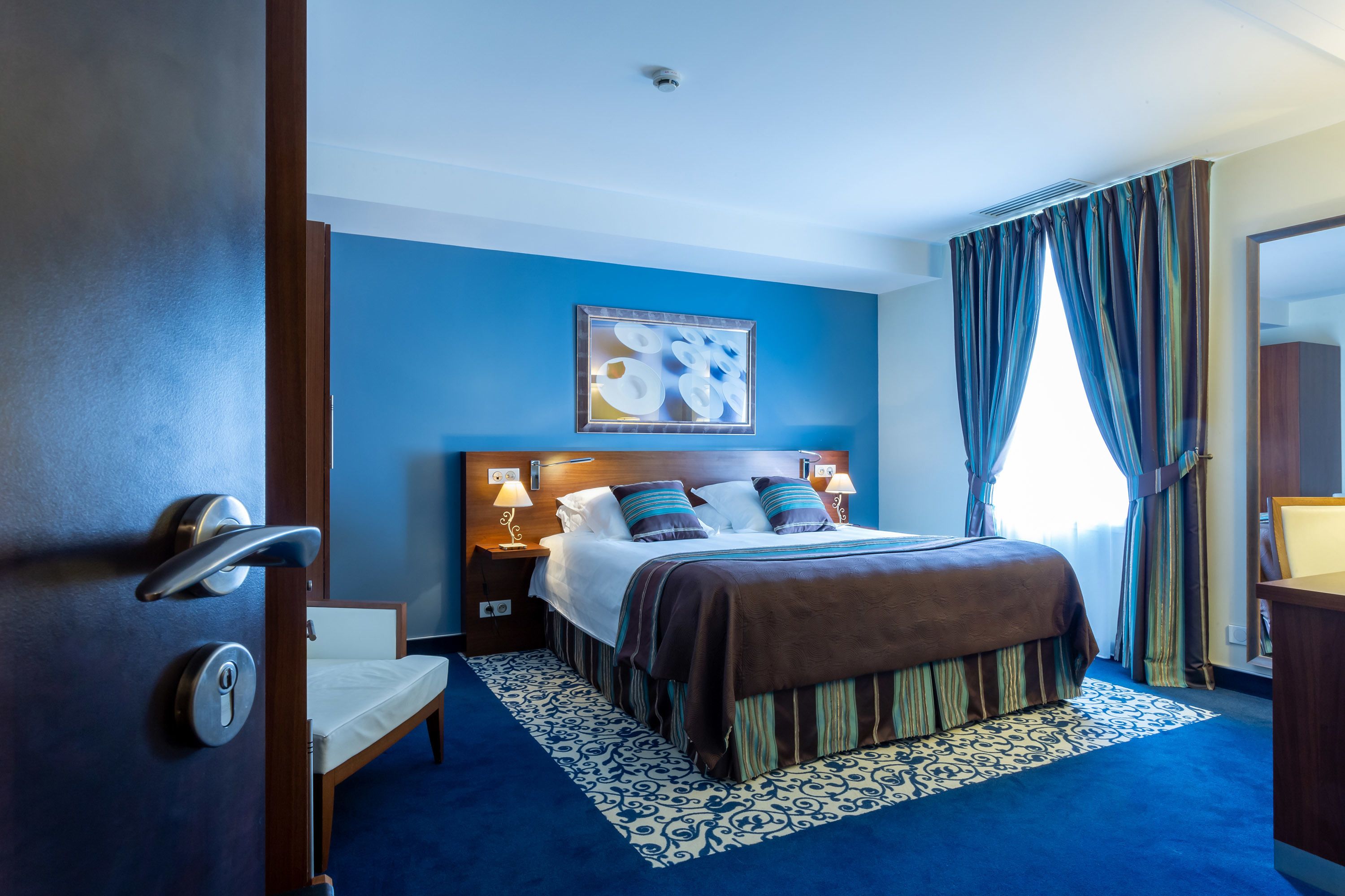 Une chambre d’hôtel avec un lit, une table de chevet, une chaise, un bureau et un tableau au mur.