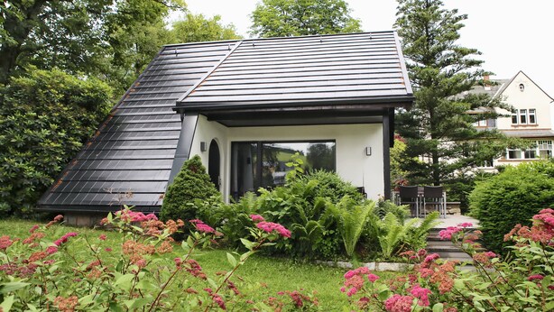A modern house with a sloped roof, surrounded by lush greenery and flowering plants. - Ferienhaus Drebach (Drebach)