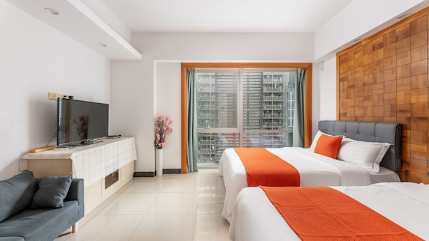 A hotel room with a bed, a sofa, a TV, and a window with a view of buildings. - Guangzhou Damei Apartment (Guangzhou)