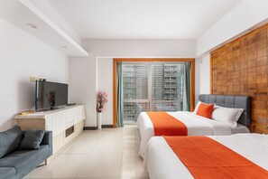A hotel room with a bed, a sofa, a TV, and a window with a view of buildings.