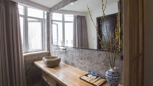 A modern bathroom with a large mirror, a wooden vanity, a stone sink, and a vase with branches.