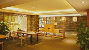 A dining area with a wooden table and chairs, a built-in bookshelf, and a stone wall.