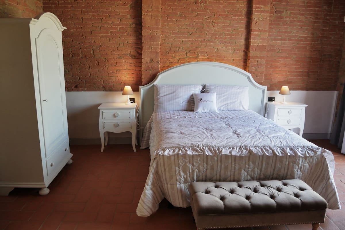 A bedroom with a bed, nightstands, a dresser, and a brick wall.