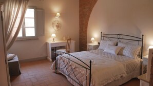 Ein Schlafzimmer mit Bett, Schreibtisch und Stuhl, mit Ziegelwand und einem Fenster mit Vorhängen.