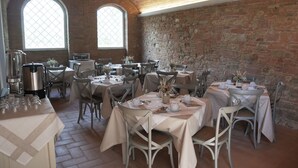Ein Restaurant mit mehreren Esstischen, ausgestattet mit einer rustikalen Ziegelwand und hohen Bogenfenstern.