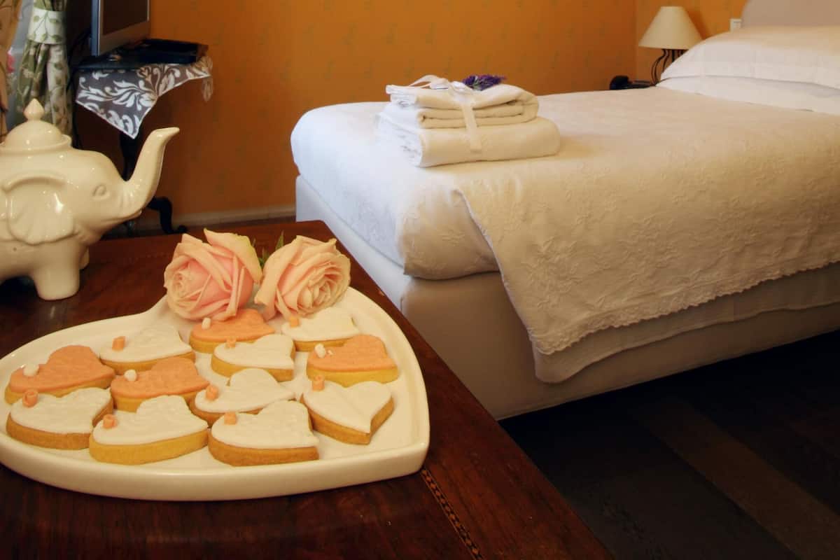 A hotel room with a bed, a bedside table with a lamp, a television, and a tray of heart-shaped cookies.