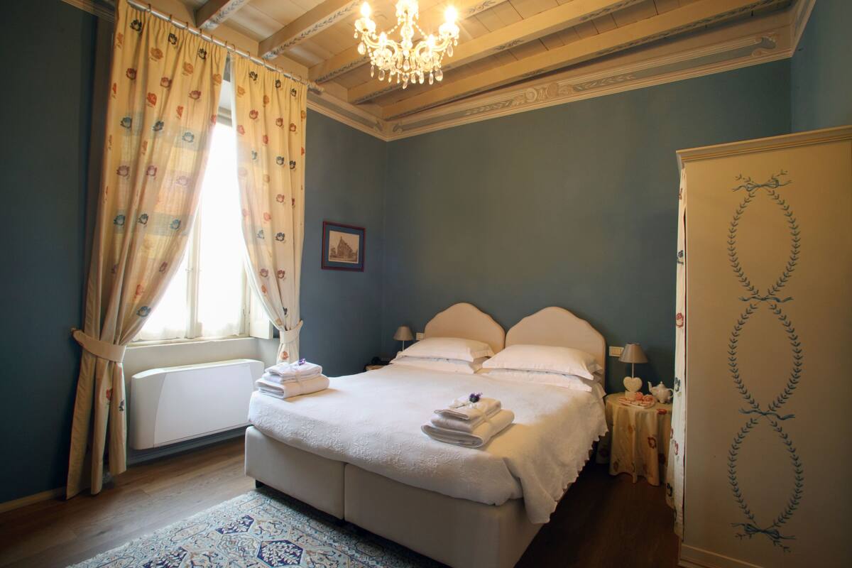 A bedroom with a large bed, a radiator, a chandelier, and a decorative wall design.