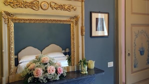 A bedroom with a large ornate mirror, a bed with white linens, a bouquet of flowers, and a framed picture on the wall. - Villa Valentina (Tradate)
