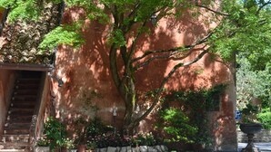 A building with a red brick exterior, a large tree in front, and a stone wall with a planter. - Villa Valentina (Tradate)