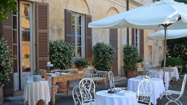 An outdoor dining area with tables and chairs, a wooden table with food and drinks, and a large umbrella. - Villa Valentina (Tradate)