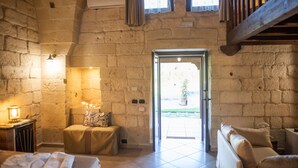 A stone-walled room with a bed, a small table with candles, and a bench. - Masseria Giamarra (Carpignano Salentino)
