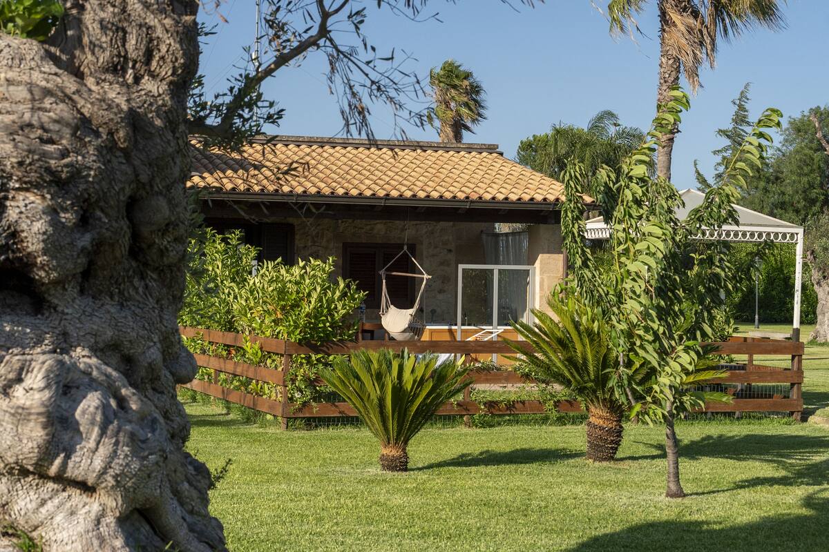 A house with a tiled roof, a hammock, and a fenced garden area with palm trees.
