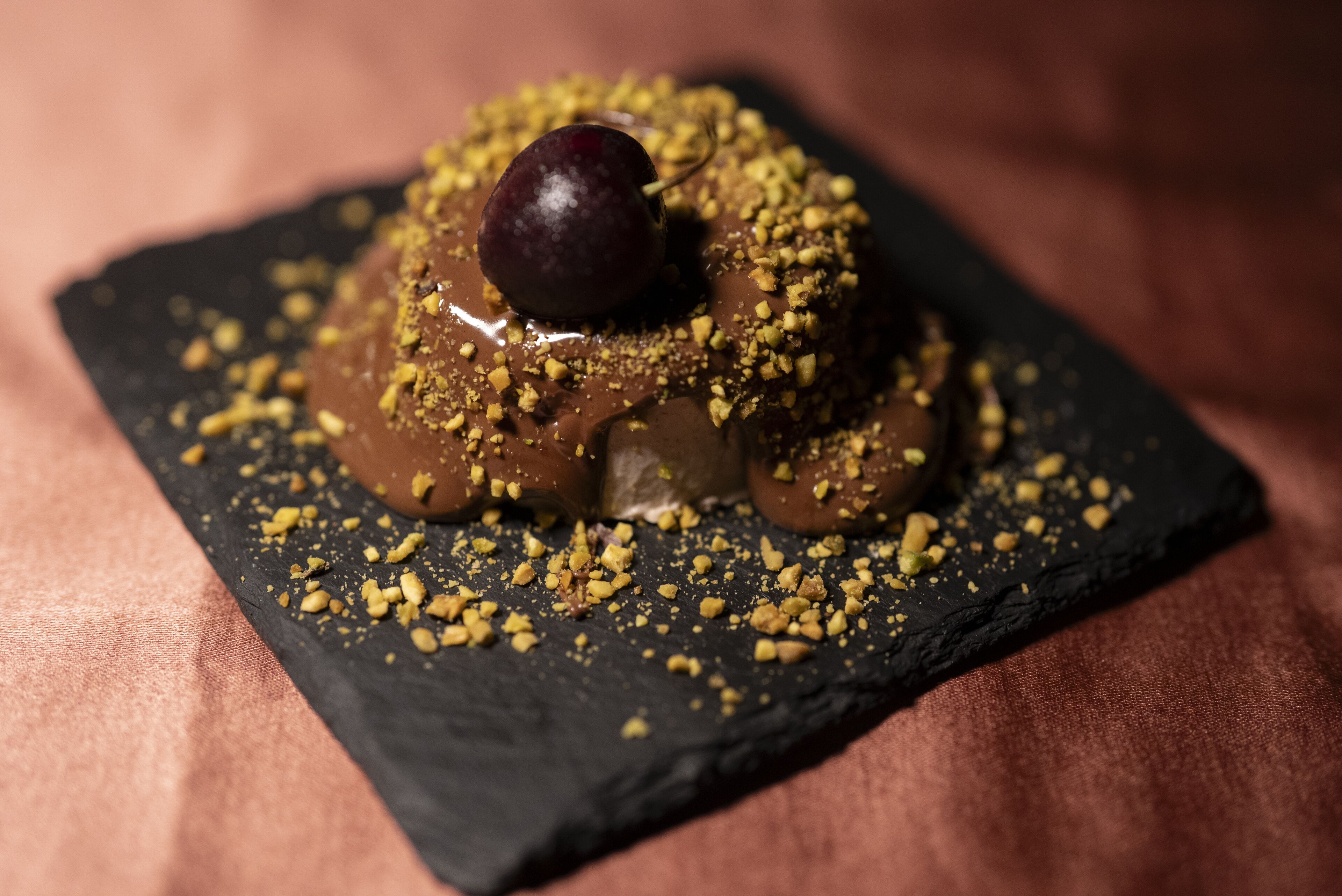 Dessert auf einer Schieferplatte mit gemahlenen Nüssen und einer Kirsche.