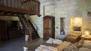 A rustic room with a wooden staircase, a large wooden cabinet, a bed with towels, a nightstand with a lamp, and a stone wall. - Masseria Giamarra (Carpignano Salentino)