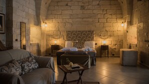 A cozy room with a stone wall, a bed, a sofa, and a small table with a lamp. - Masseria Giamarra (Carpignano Salentino)