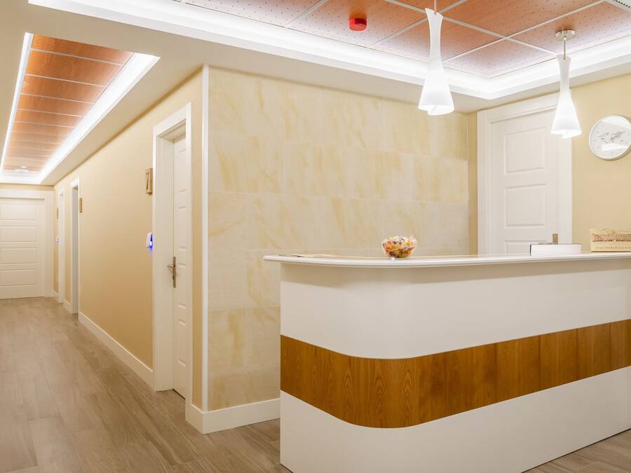 A hotel reception area with a wooden counter, a clock on the wall, and a ceiling with recessed lighting.