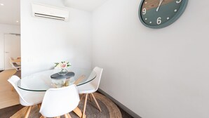 Une pièce moderne avec une table en verre, des chaises blanches, une horloge et un appareil de climatisation.