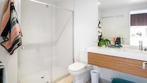 Une salle de bain moderne avec une douche à parois de verre, des toilettes blanches et un meuble-lavabo en bois avec un évier et un miroir.
