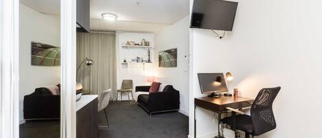A hotel room with a desk, chair, TV, and a bed.