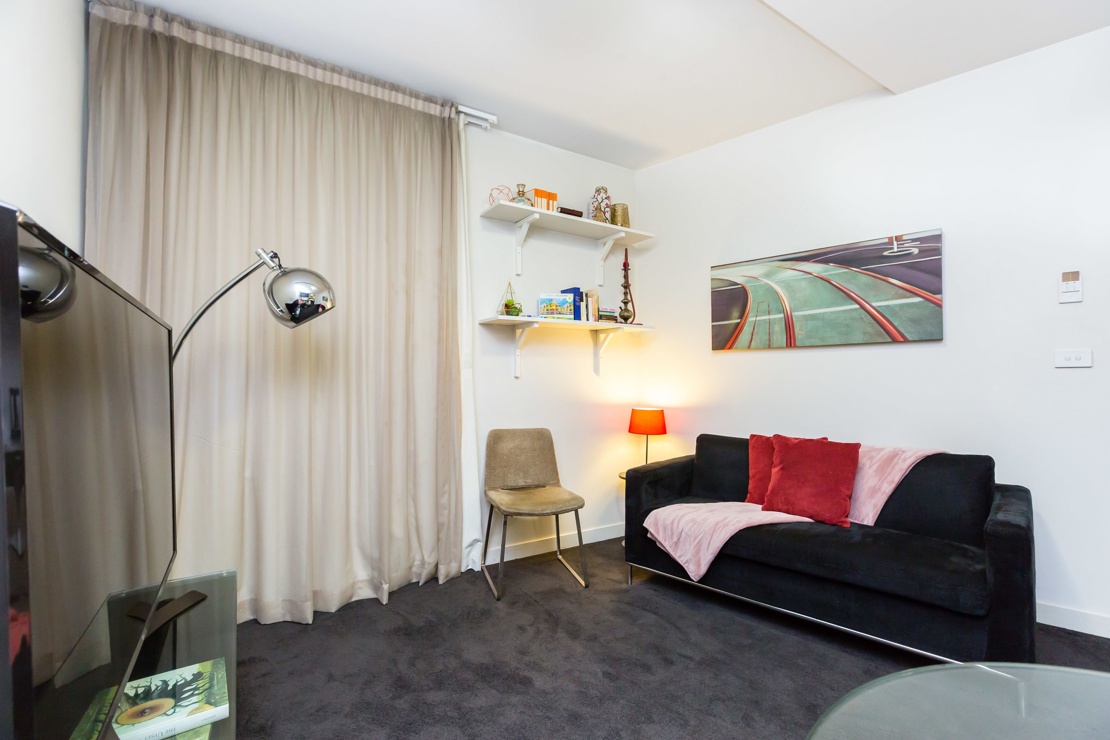Un salon moderne avec un canap é noir, une table basse en verre, un fauteuil, un bureau avec une lampe et une bibliothèque.
