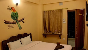 A hotel room with a bed, a wall mural of a bird, a window with curtains, and a door. - Quetzel Guest House (Pokhara)