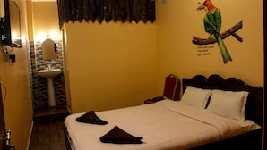 A hotel room with a bed, a nightstand, a mirror, a sink, and a wall mural of a bird. - Quetzel Guest House (Pokhara)