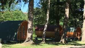 A row of wooden cabins with attached porches, surrounded by trees. - Camping Le Parc les Atypiques (Availles-Limouzine)